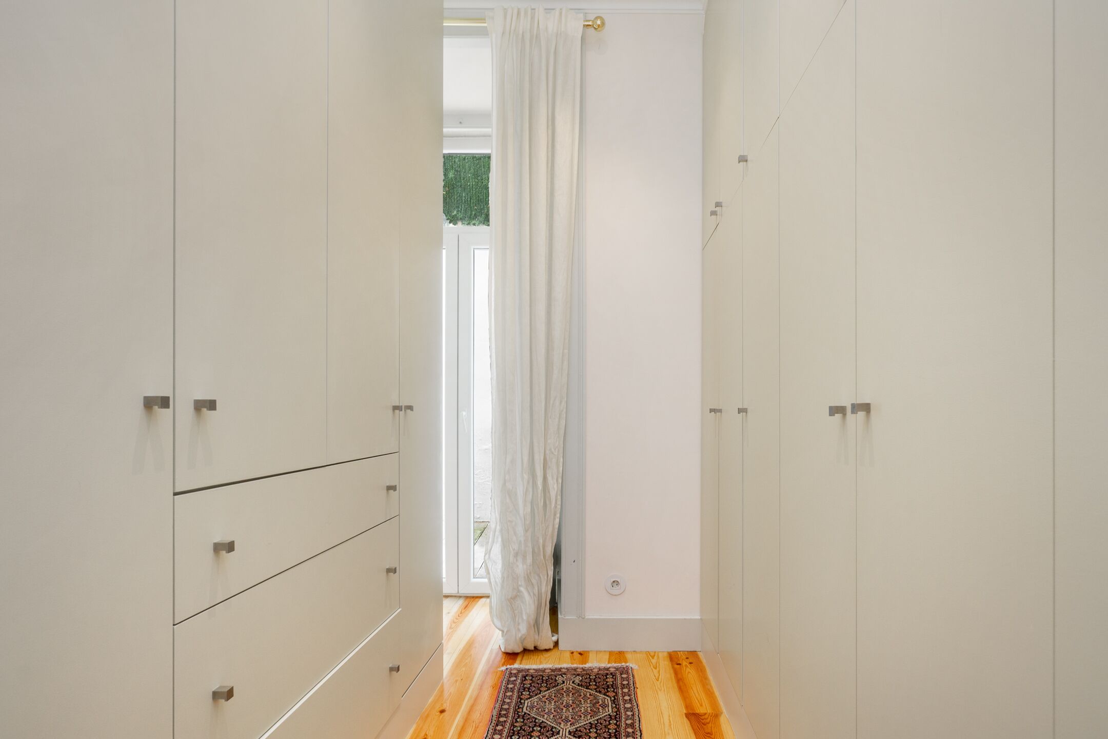 A narrow hallway with white cabinets, a wooden floor, and a patterned rug.