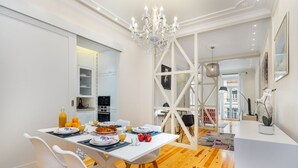 A modern dining area with a white table set for breakfast, wooden flooring, and a chandelier. - Luxury Stay In Prime Location W/ Ac, Lift & Private Patio (Lisbon)