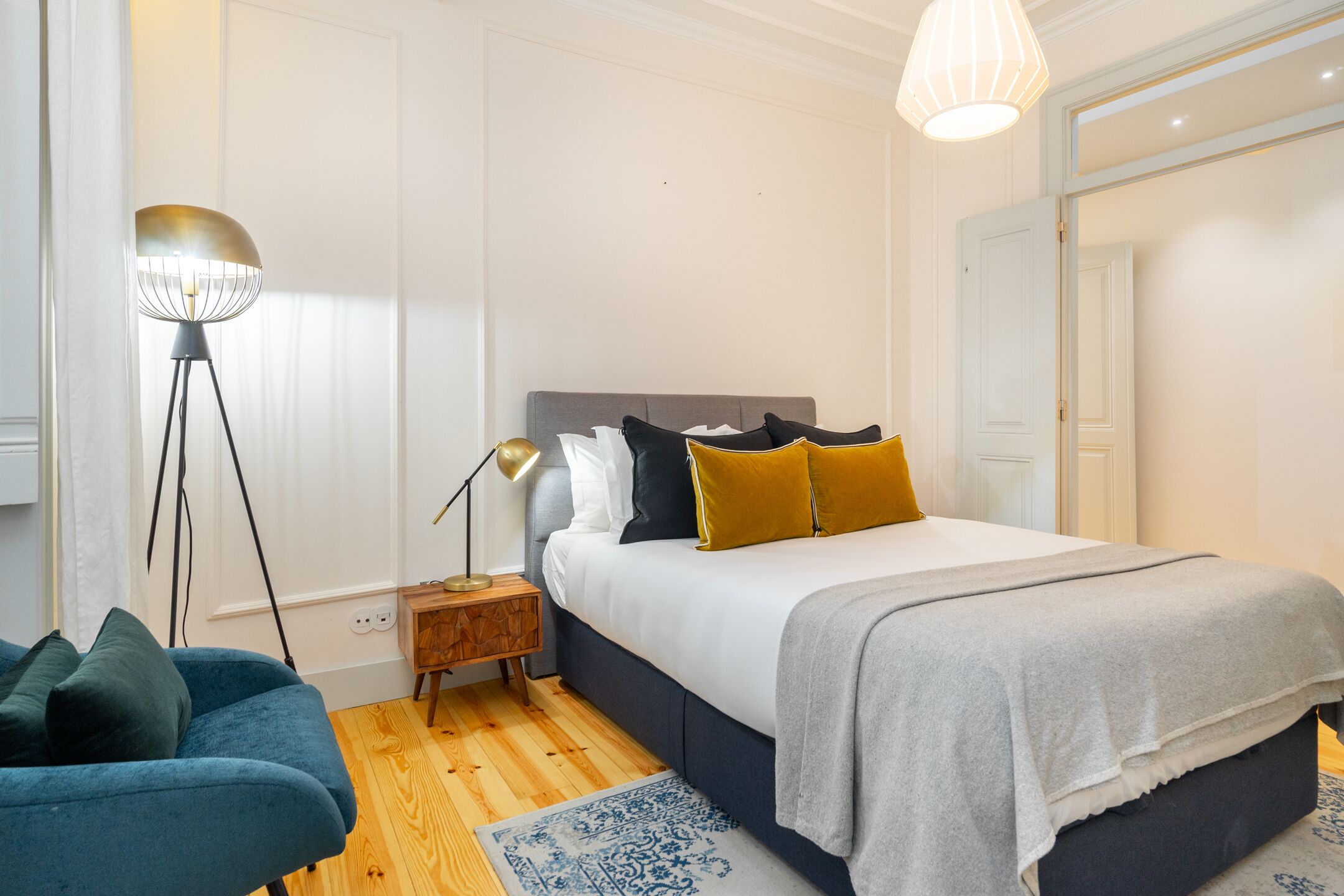 Et soveværelse med seng, sengebord, lampe og en blå stol.