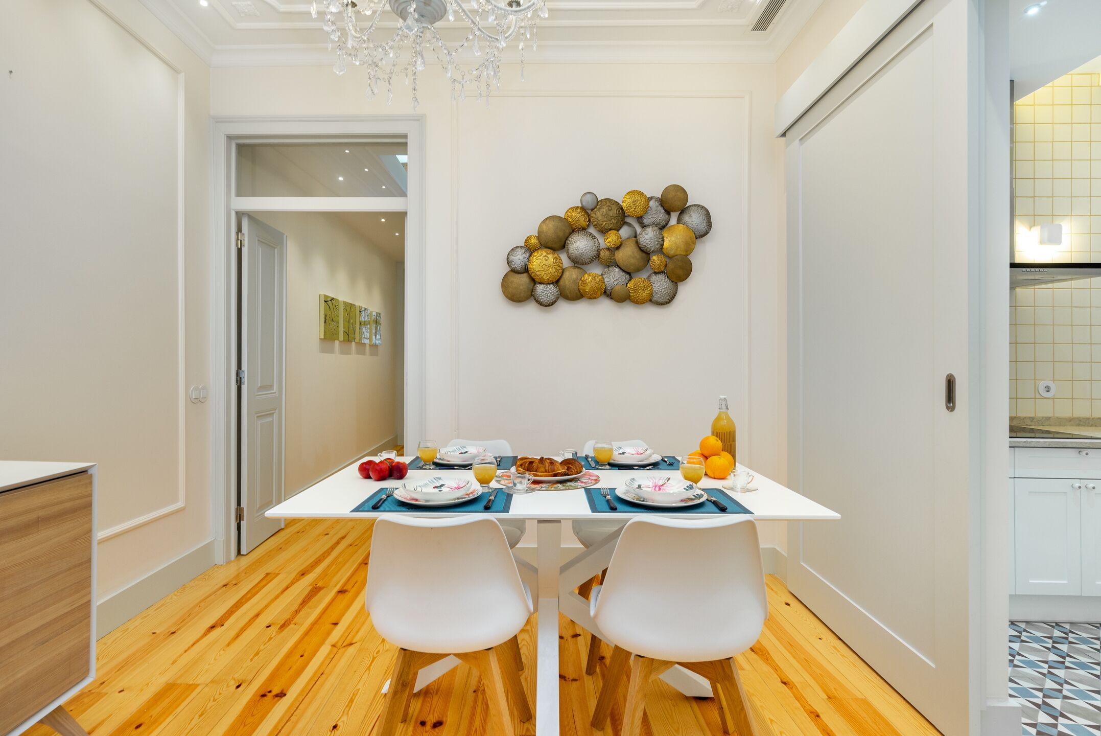 A dining area with a white table set for two, wooden flooring, and a decorative wall piece.