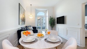 Comedor con una mesa redonda dispuesta para cuatro personas, una araña, un televisor de pantalla plana y vista de la ciudad a través de un arco.