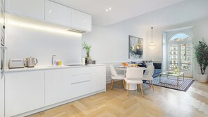 Una cocina moderna con armarios blancos, un comedor con mesa de vidrio y vistas a la ciudad a través de un gran ventanal.