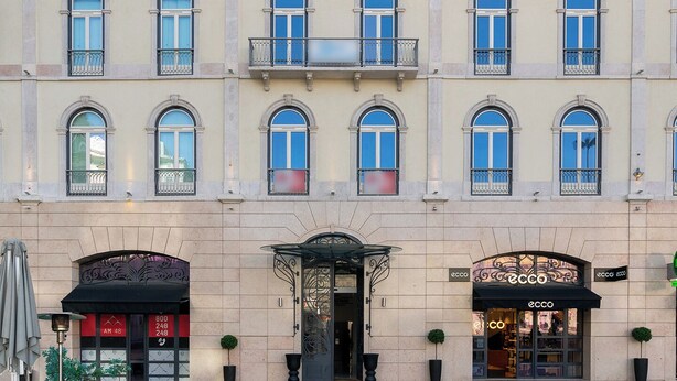 Un edificio de varios pisos con entrada central, balcones y un local comercial con un letrero.