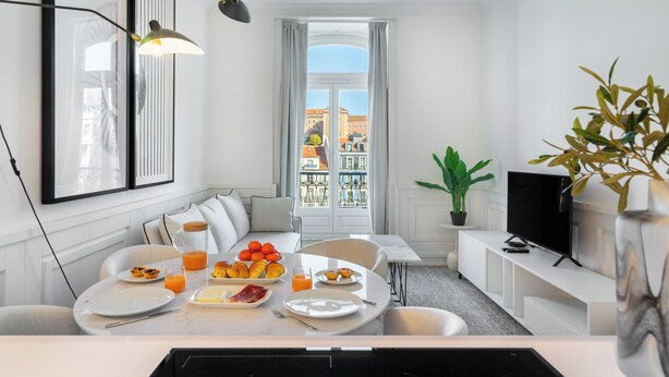 A modern, well-lit room with a dining table set for breakfast, a sofa, a TV, and a balcony with a view of buildings. - The Boulevard Prime Location W/ Elevator (Lisbon)