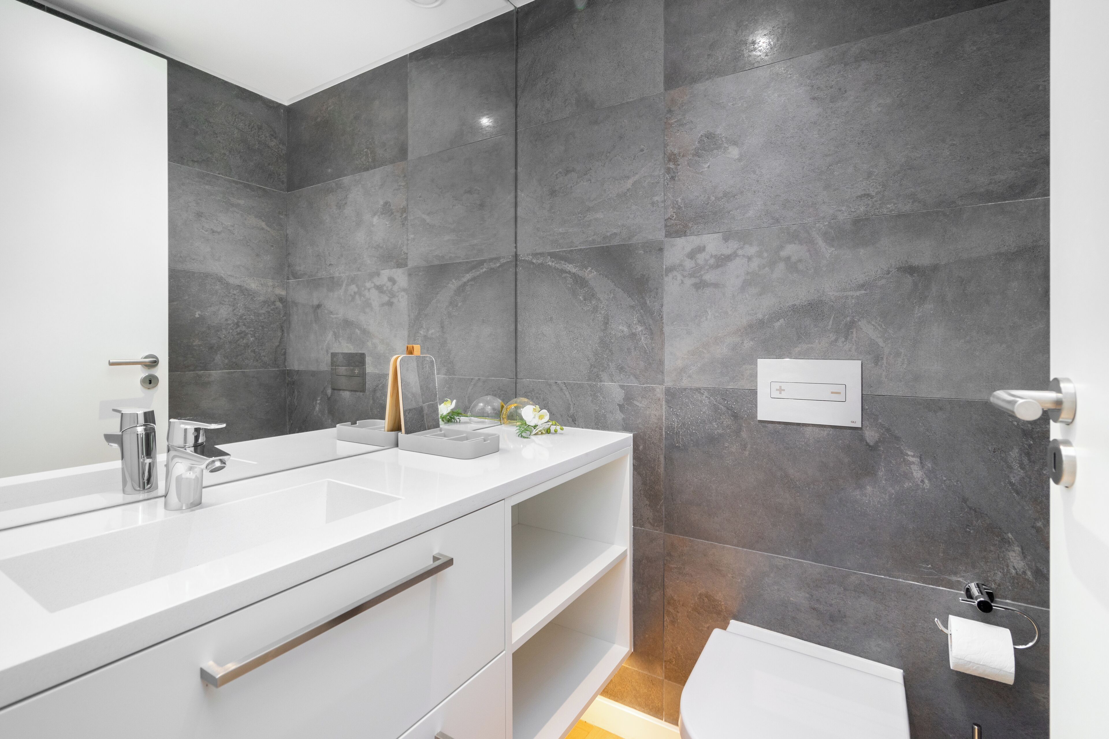 A modern bathroom with a large mirror, two sinks, and a toilet.