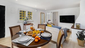 Un salon moderne comprenant un coin repas, un téléviseur à écran plat fixé au mur et une grande fenêtre aux cadres jaunes.