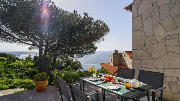 Un espace extérieur aménagé pour prendre les repas, avec une table dressée pour deux personnes, offrant une vue panoramique sur la mer.