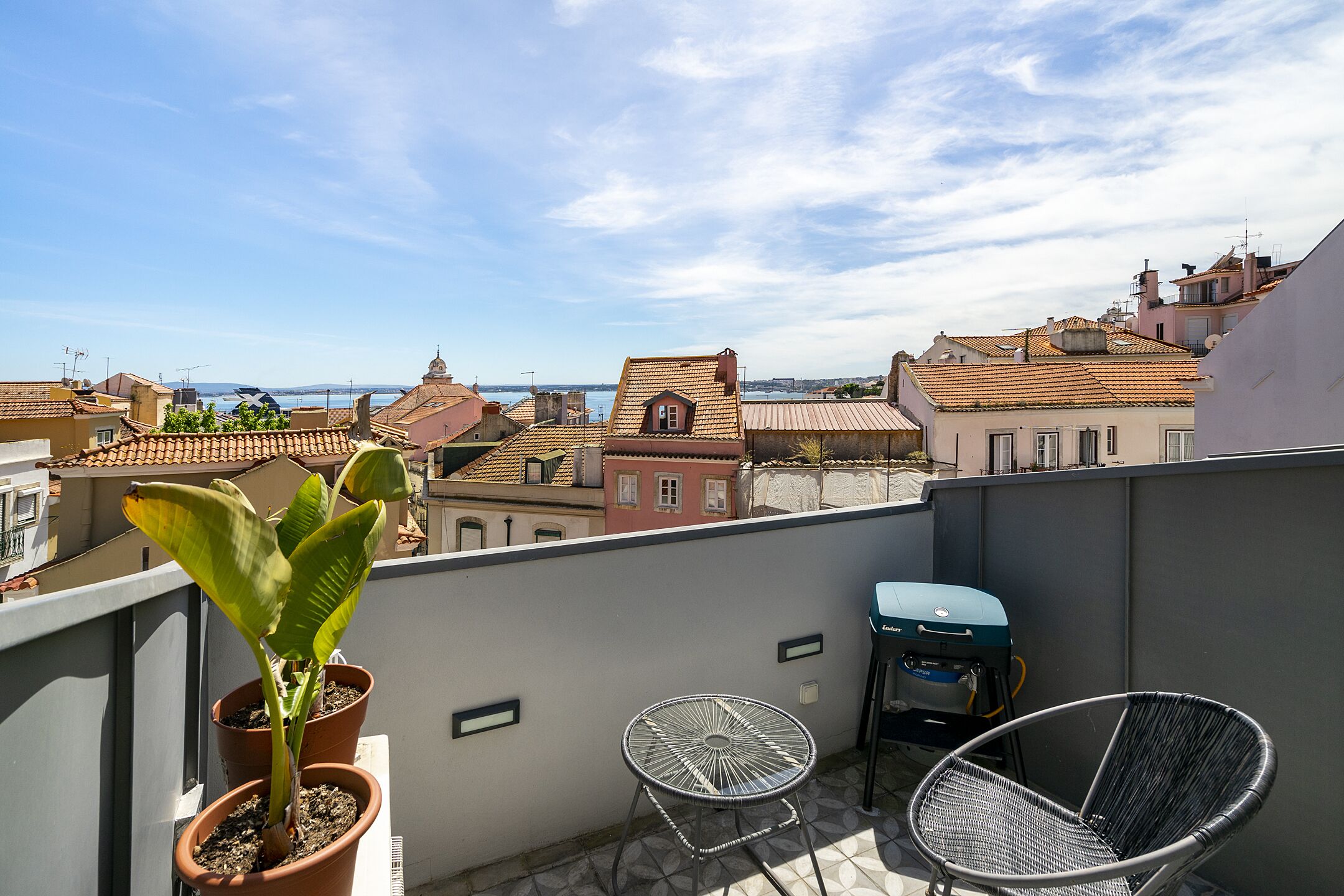 A balcony with potted plants, a grill, and two chairs.