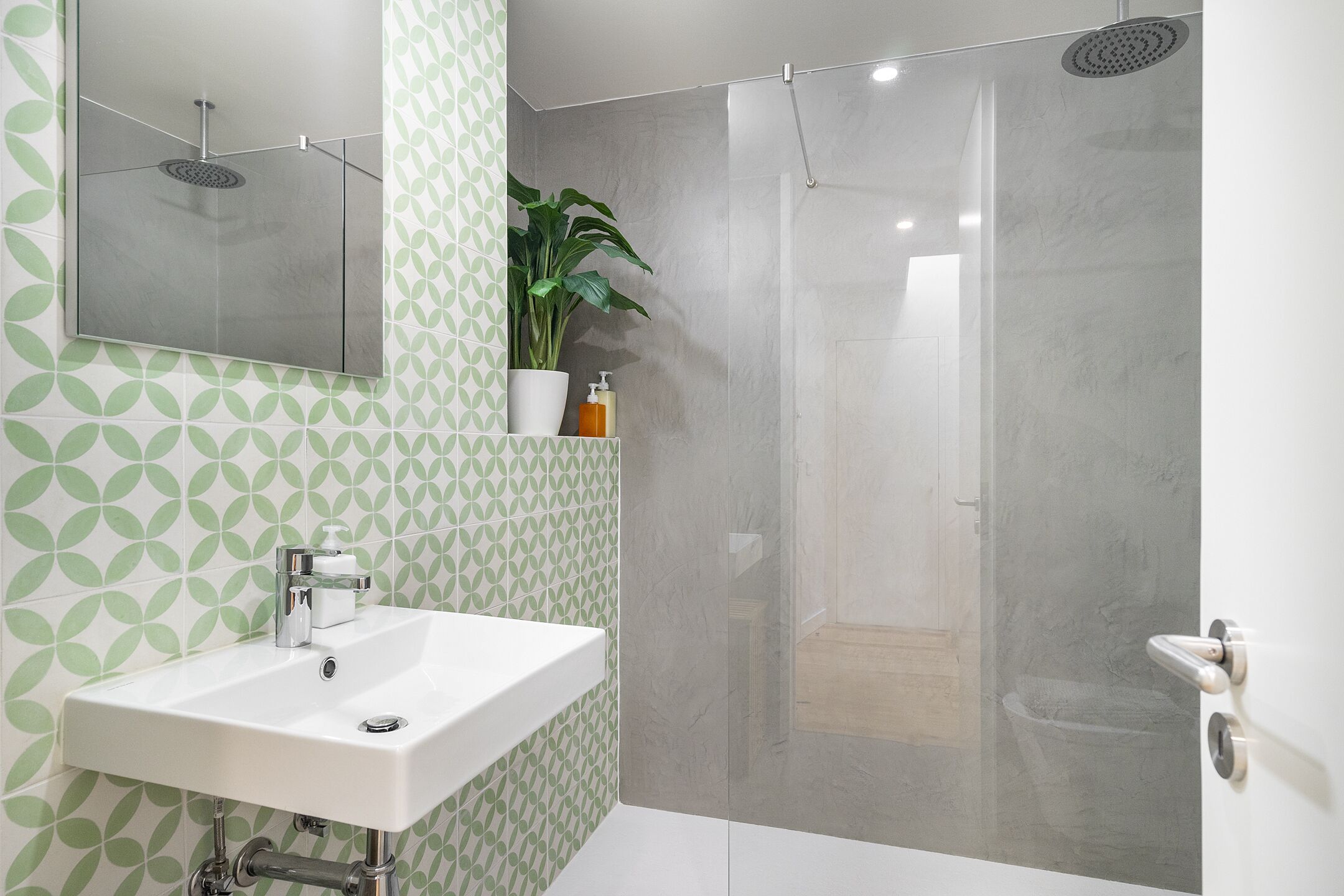 Un bagno con un lavandino bianco, uno specchio, una doccia e una parete decorata con un motivo verde.