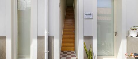 A building entrance with a wooden staircase, a potted plant, and a doormat.
