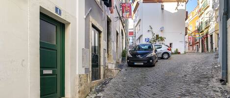 A narrow cobblestone street with buildings on either side, a green door, and parked cars.