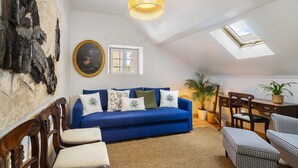 Ein gemütliches Wohnzimmer mit einem blauen Sofa, Holzstühlen, einem gemusterten Teppich und einer Deckenleuchte.