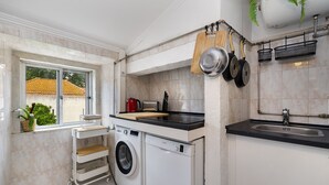 Eine kleine Küche mit Waschmaschine, Spüle und einem Fenster mit Blick auf ein Haus.