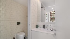 A modern bathroom with white subway tiles, a white toilet, a sink with a mirror, and a shower area. - Lisbon'S Elite A Stylish & Modern Studio W Patio (Lisbon)