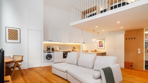 Ein modernes Wohnzimmer mit einer Couch, Holzboden, einem Essbereich und einer Küche im Hintergrund.