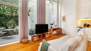 Ein modernes Wohnzimmer mit großem Fernseher, Holzmöbeln und Blick auf einen Garten durch große Fenster.