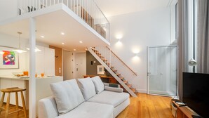 Ein modernes Wohnzimmer mit Sofa, Holzboden, Fernseher und einer Treppe zu einer oberen Ebene.