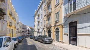 Eine Kopfsteinpflasterstraße gesäumt von mehrstöckigen Gebäuden, mit geparkten Autos und blauem Himmel.