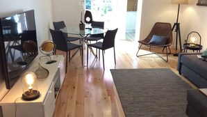 Un soggiorno moderno con un tavolo da pranzo in vetro, sedie scure, un divano, una TV e una lampada.