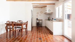 A kitchen with a tiled floor, wooden beams, a dining table with chairs, and a window with a view. - Countryside Charm Near Wedding Venue W/ Bbq Patio (Torres Vedras)