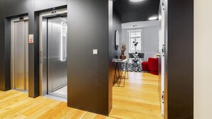 A modern elevator with a control panel, a wooden floor, and a dining area with a red chair and a table. - Prime Location Contemporary Luxury Apartment W/ Ac & Elevator (Lisbon)