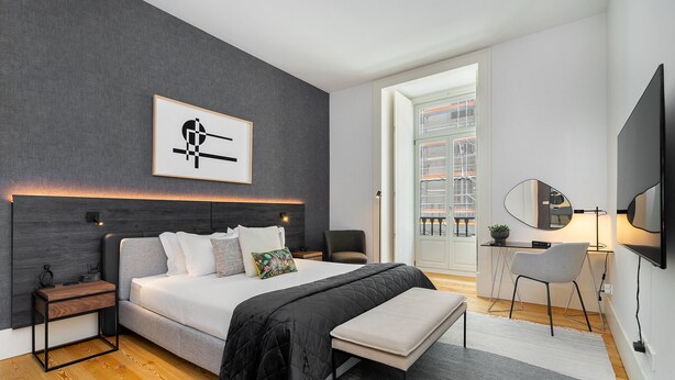 A modern bedroom with a large bed, bedside tables, a bench, a desk with a chair, a TV, and a framed artwork on the wall. - Prime Location Contemporary Luxury Apartment W/ Ac & Elevator (Lisbon)