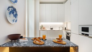 A modern kitchen with white cabinets, a marble countertop, and a built-in oven. There are two stools at the counter and a bowl on the left. - Prime Location Contemporary Luxury Apartment W/ Ac & Elevator (Lisbon)