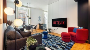 A modern living room with a red sofa, a brown couch, and a blue accent chair. A flat-screen TV mounted on the wall displays the Netflix logo. - Prime Location Contemporary Luxury Apartment W/ Ac & Elevator (Lisbon)