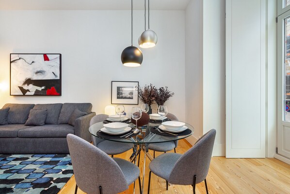 A modern living room with a gray sofa, a glass dining table with four chairs, and two pendant lights. - Prime Location Contemporary Luxury Apartment W/ Ac & Elevator (Lisbon)
