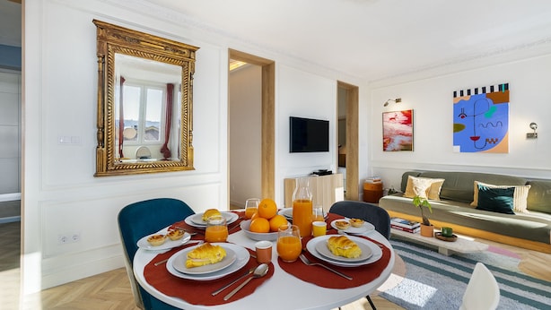 A dining area with a table set for breakfast, a sofa, and artwork on the walls. - Historic Centre Modern Masterpiece W River Views (Lisbon)