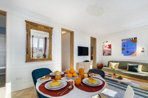 A dining area with a table set for breakfast, a sofa, and artwork on the walls. - Historic Centre Modern Masterpiece W River Views (Lisbon)