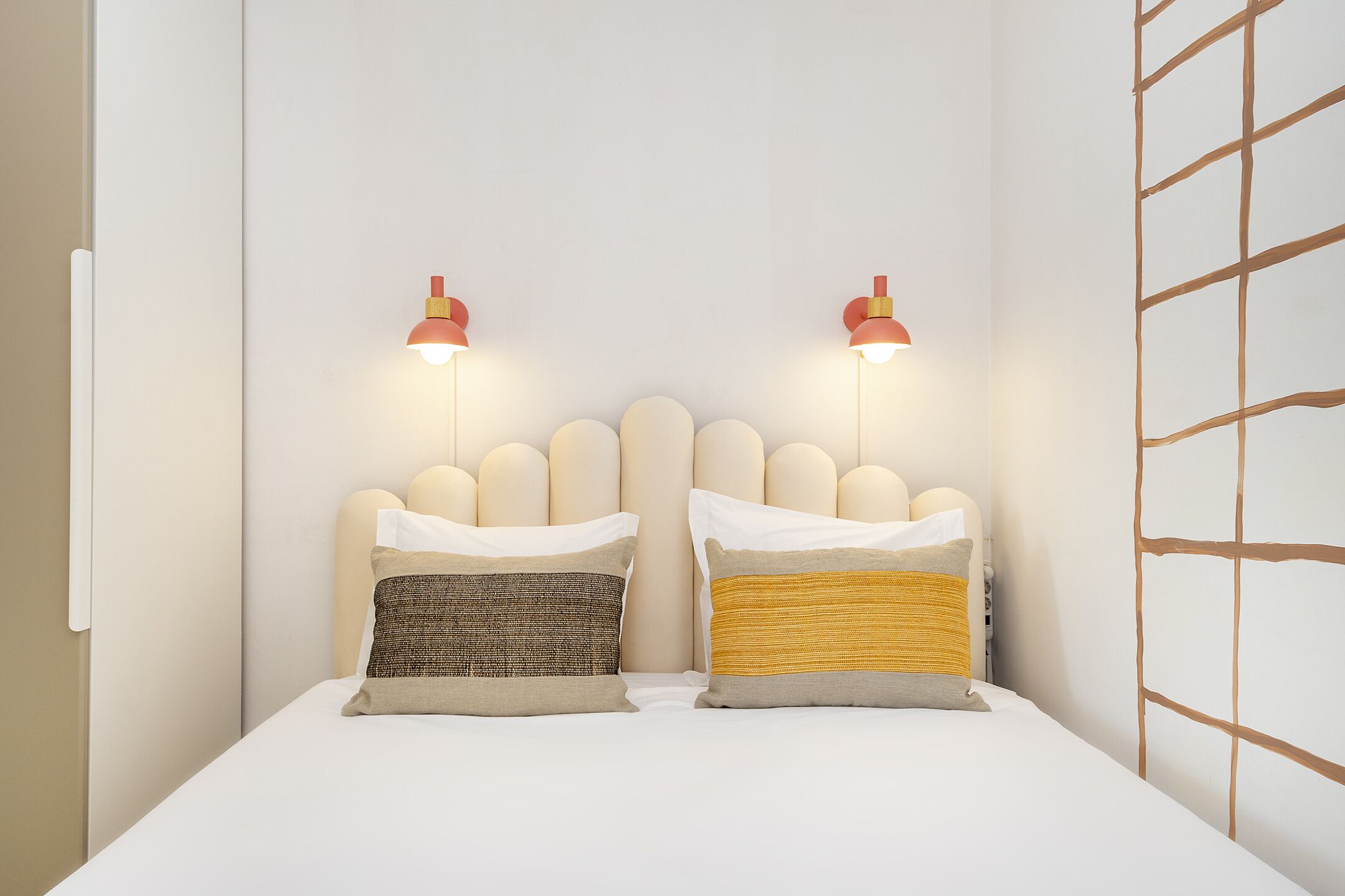 A neatly made bed with two pillows, a headboard with a unique design, and two wall-mounted lamps.