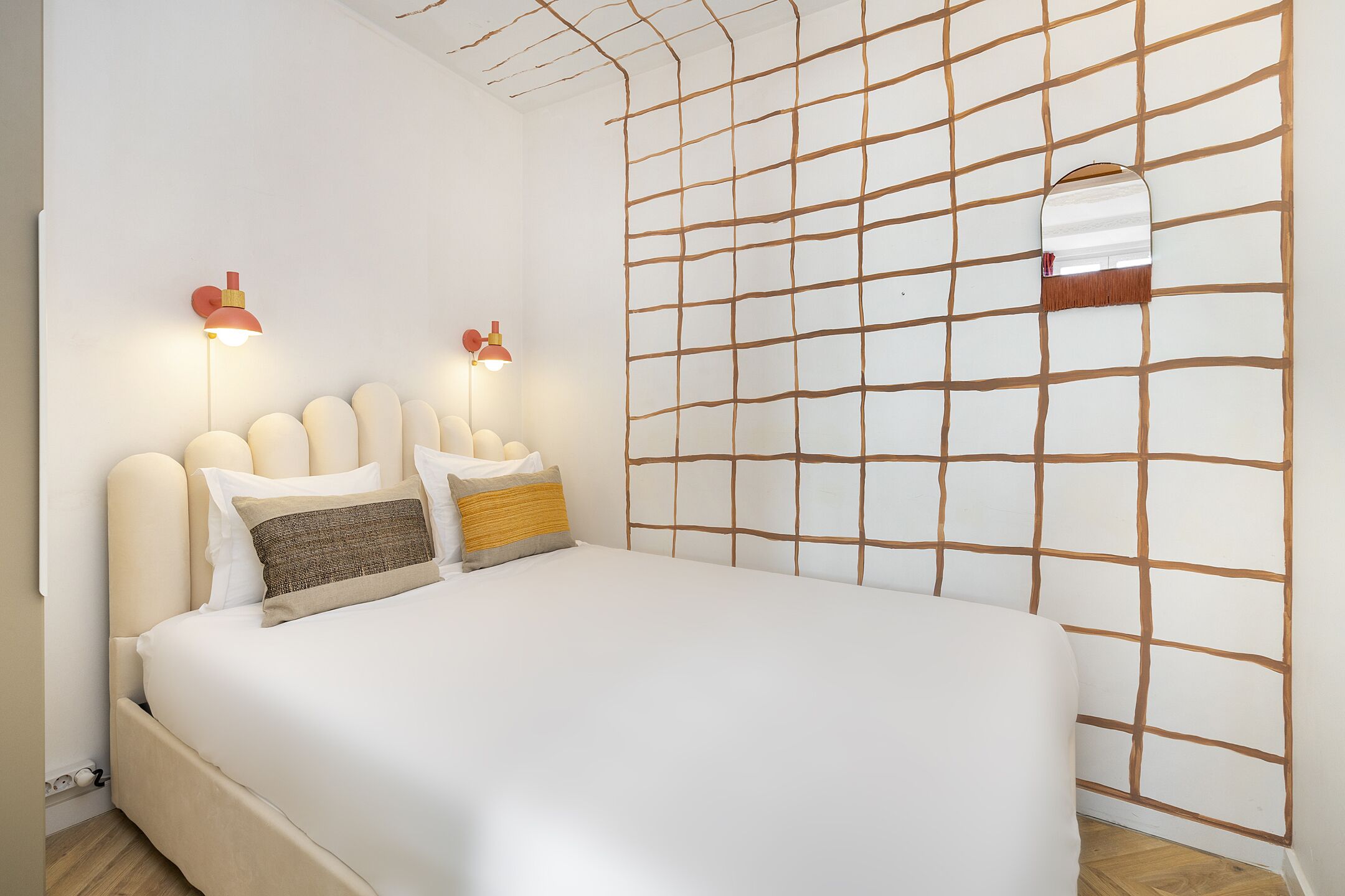 A neatly made bed with a headboard, two wall-mounted lamps, and a grid-patterned wall.