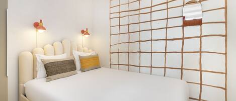 A neatly made bed with a headboard, two wall-mounted lamps, and a grid-patterned wall.