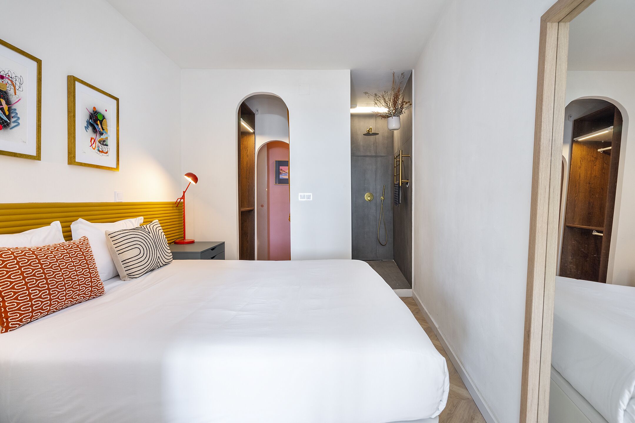 Et hotelværelse med en stor seng, et natbord, en rød lampe og et bruseområde.