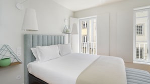 Un dormitorio moderno con cama, lámpara de noche y ventana con vista a edificios.