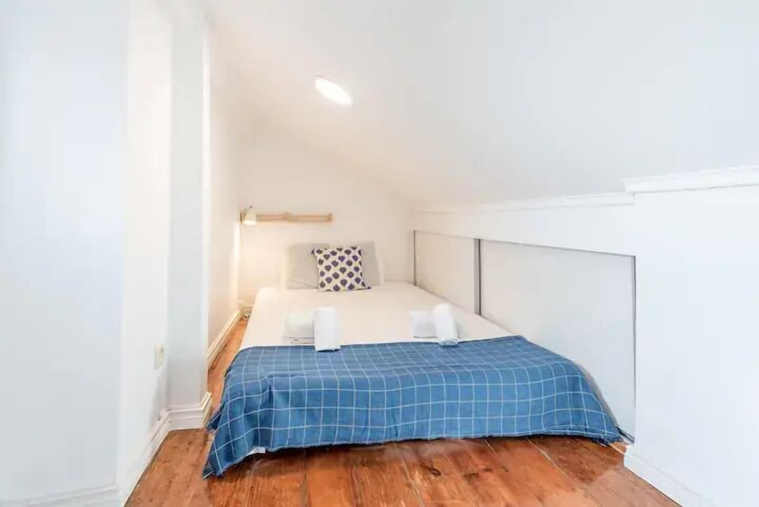 A small, neatly arranged bedroom with a bed, a bedside table, and a wall-mounted light fixture.