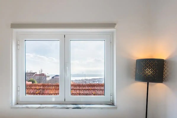 A room with a large window overlooking a cityscape and a lamp on the wall. - The Loft In Principe Real (Lisbon)