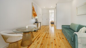 Un salon moderne avec une table basse en verre, des fauteuils en osier, un canapé vert et un plancher en bois.