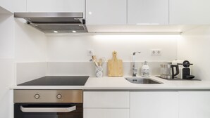 Une cuisine moderne avec des meubles blancs, une hotte en acier inoxydable, une plaque de cuisson à induction noire, un évier et une machine à café.