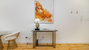 Une pièce avec une table en verre, deux chaises blanches, une table en métal avec une lampe, et un grand tableau abstrait accroché au mur.