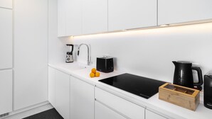 A modern kitchen with white cabinetry, a black induction cooktop, a coffee maker, a kettle, and a wooden storage box. - History and Comfort Luxurious Living in Benfica (Lisbon)