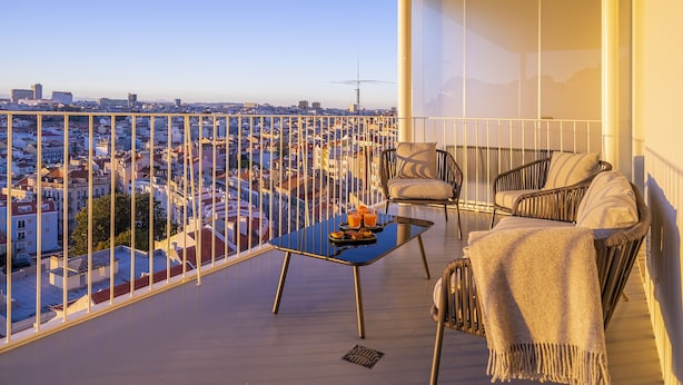 Een balkon met een glazen tafel, twee stoelen en uitzicht op een stadsgezicht.
