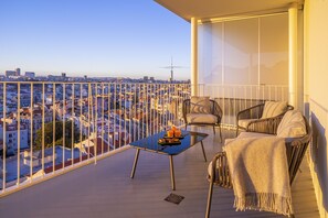 Un balcón con una mesa de vidrio, dos sillas y vistas a un paisaje urbano.