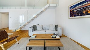 Een moderne woonkamer met een trap, een bank, een salontafel en een stadsgezicht schilderij.