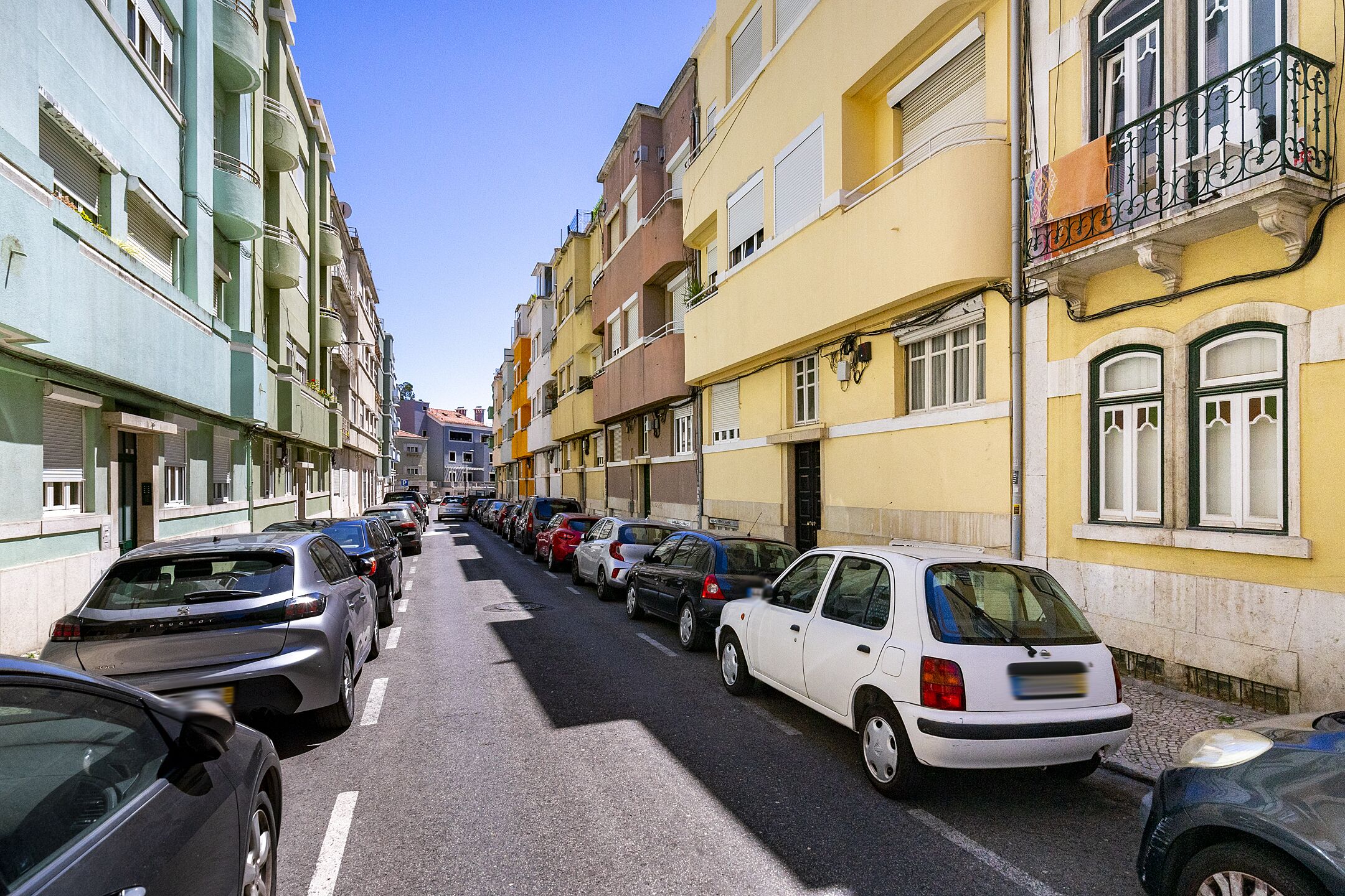 Une rue étroite bordée de voitures garées et d’immeubles aux couleurs vives.