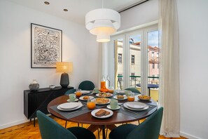 Un coin repas avec une table mise pour le petit-déjeuner, une console noire, une œuvre d’art encadrée et une vue sur les bâtiments par la fenêtre.