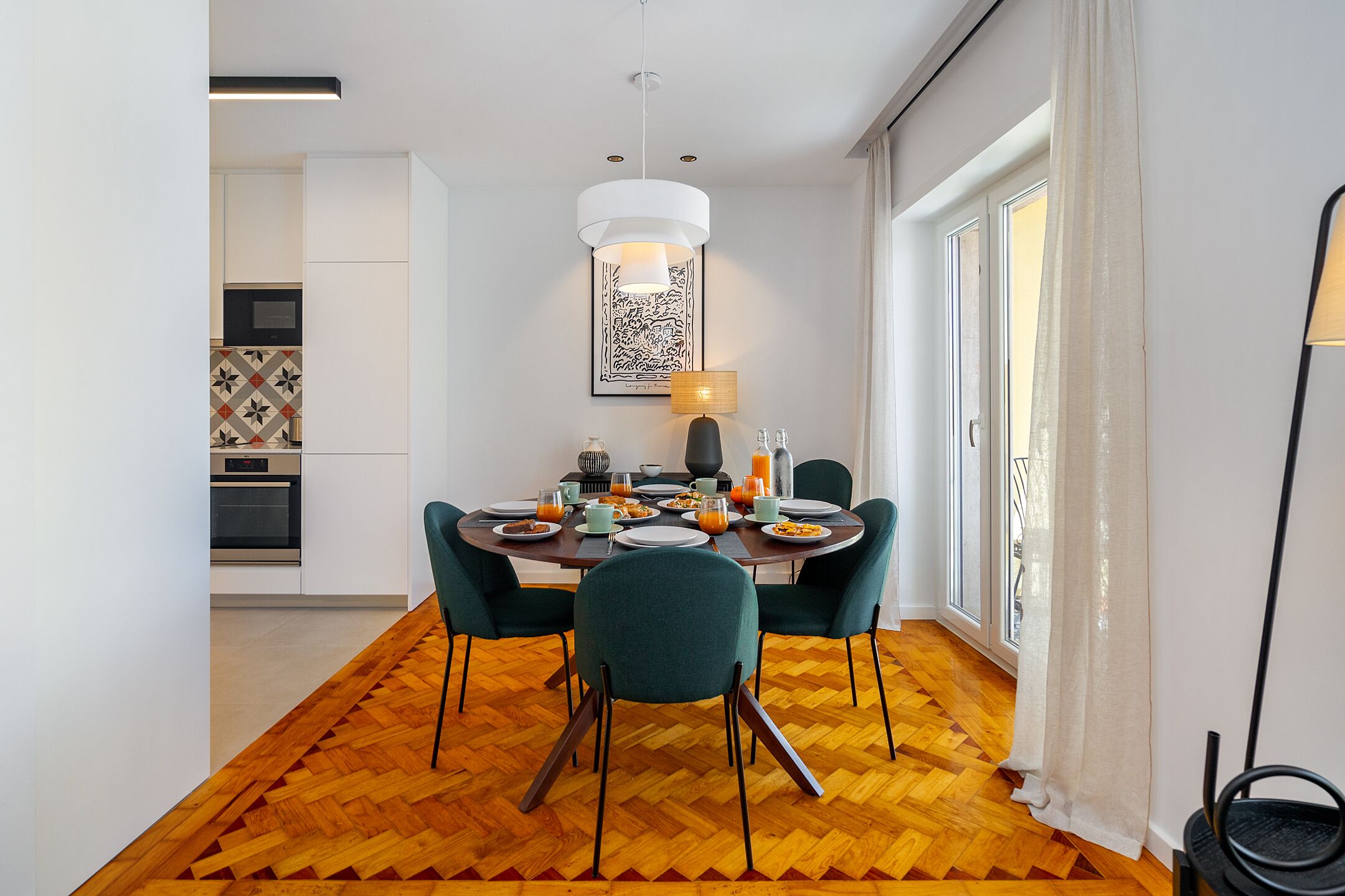 A dining area with a wooden herringbone floor, a round table, and four green chairs.
