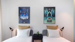 Ein Hotelzimmer mit zwei Betten, einem Nachttisch mit Pflanze und zwei Bildern an der Wand.