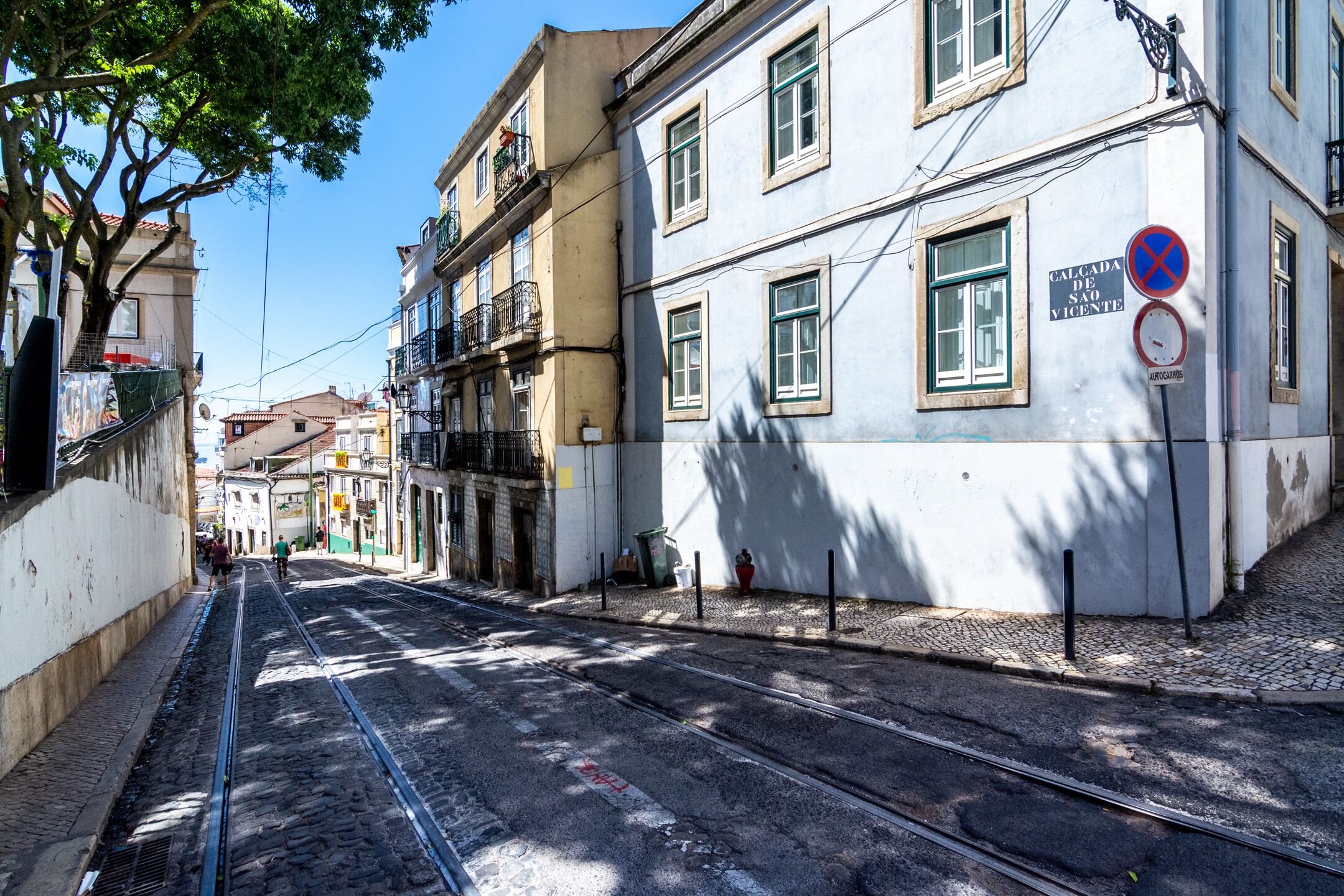 A narrow street with tram tracks, buildings with balconies, and a sign indicating a no parking zone.
